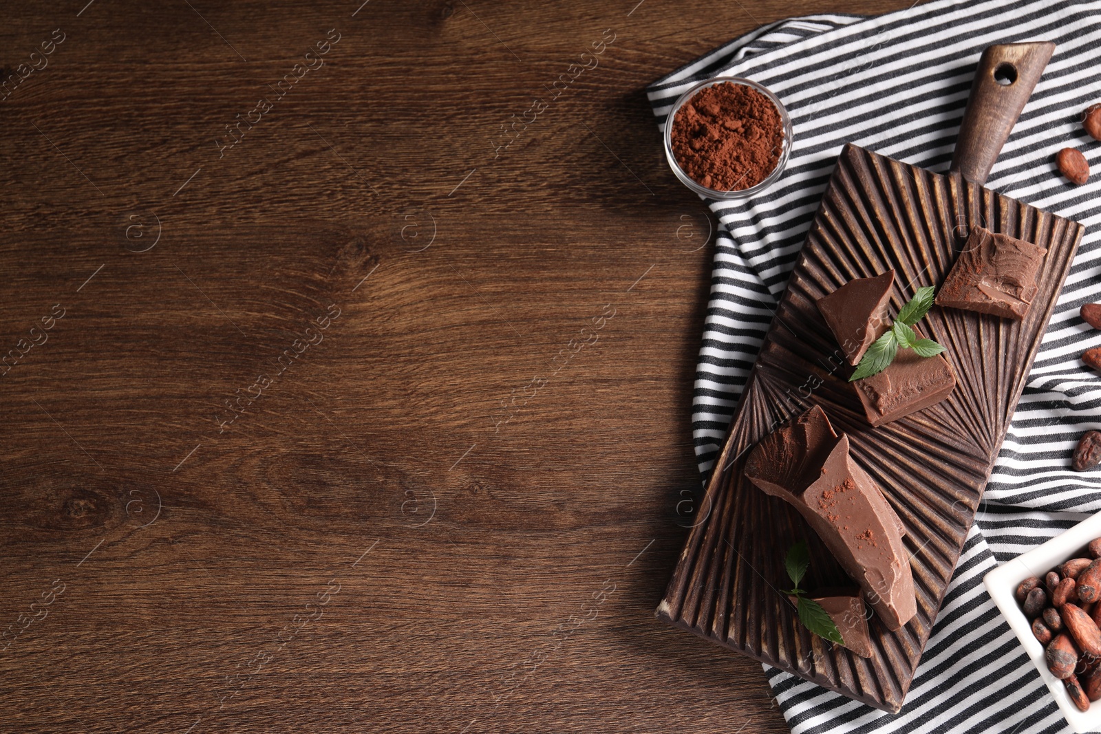 Photo of Pieces of tasty milk chocolate, cocoa beans, powder and mint on wooden table, top view. Space for text