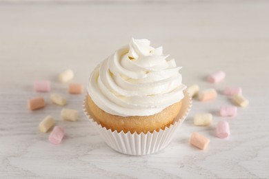 Photo of Delicious cupcake with cream and marshmallows on white wooden table, closeup
