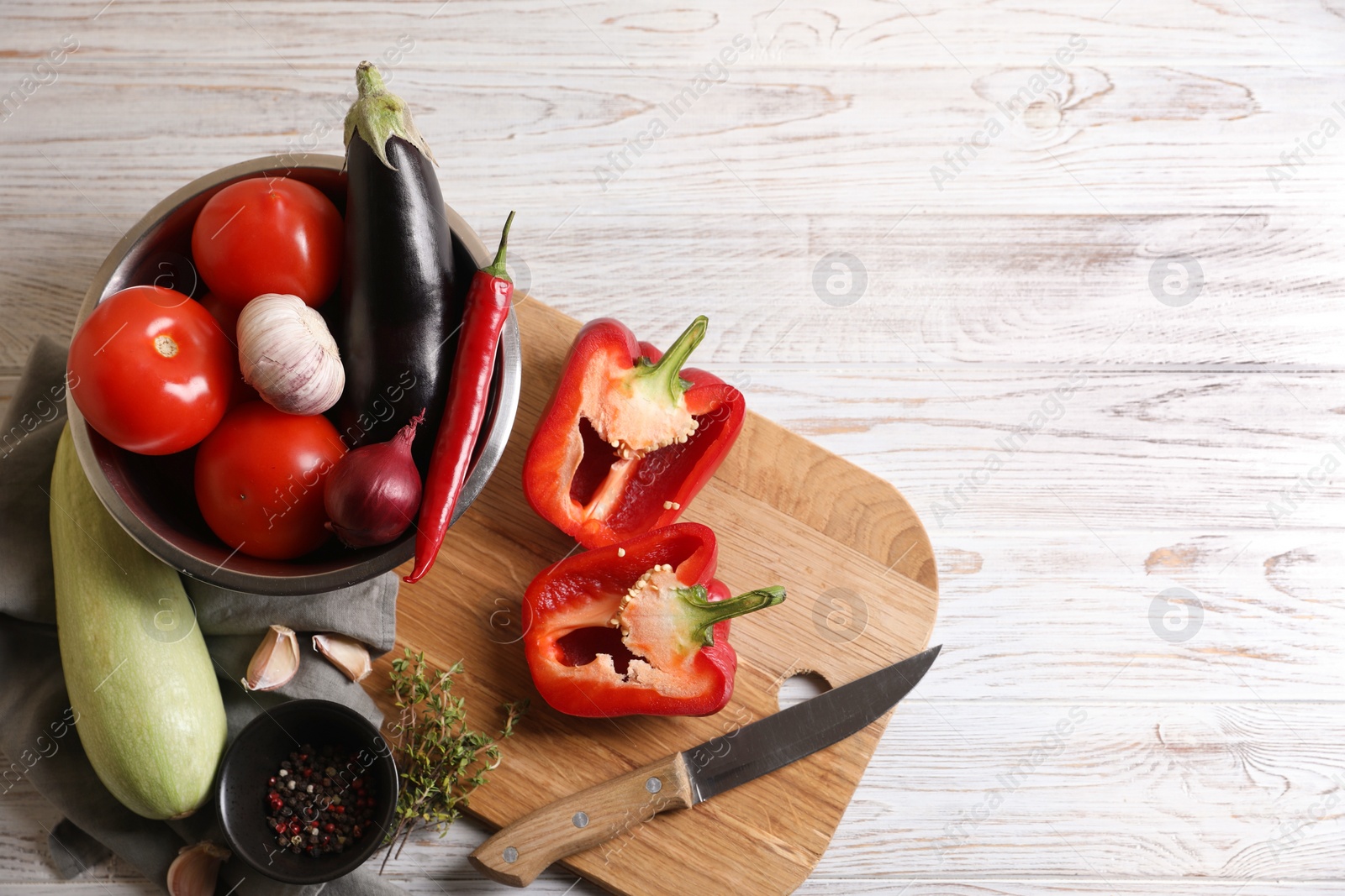 Photo of Cooking delicious ratatouille. Fresh ripe vegetables, knife and bowl on white wooden table, flat lay. Space for text