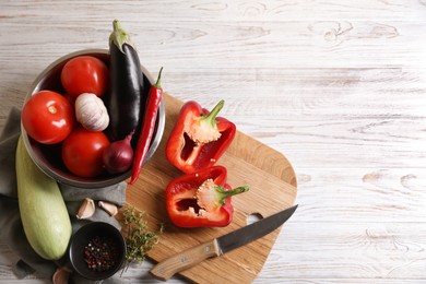 Photo of Cooking delicious ratatouille. Fresh ripe vegetables, knife and bowl on white wooden table, flat lay. Space for text