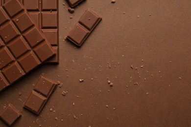 Pieces of tasty chocolate on brown background, flat lay. Space for text