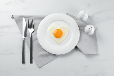 Photo of Heart shaped fried egg served on white marble table, flat lay