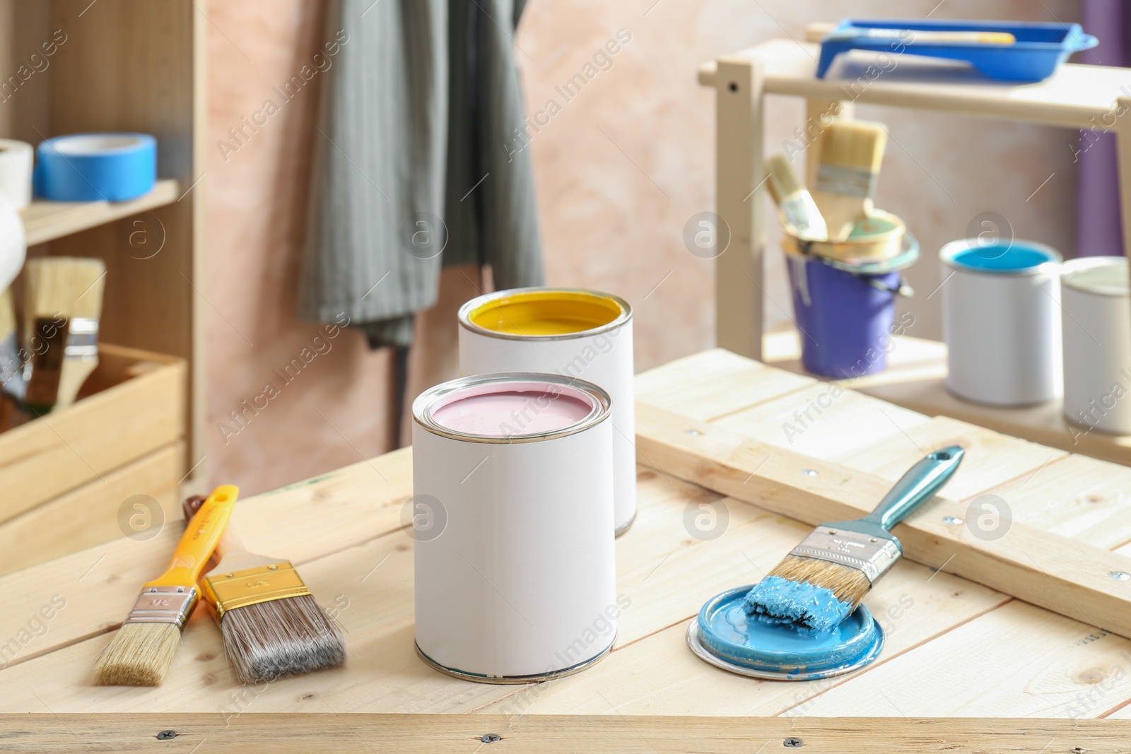 Photo of Cans of colorful paints and brushes on wooden table indoors