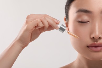 Photo of Beautiful young woman applying cosmetic serum onto her face on white background, closeup
