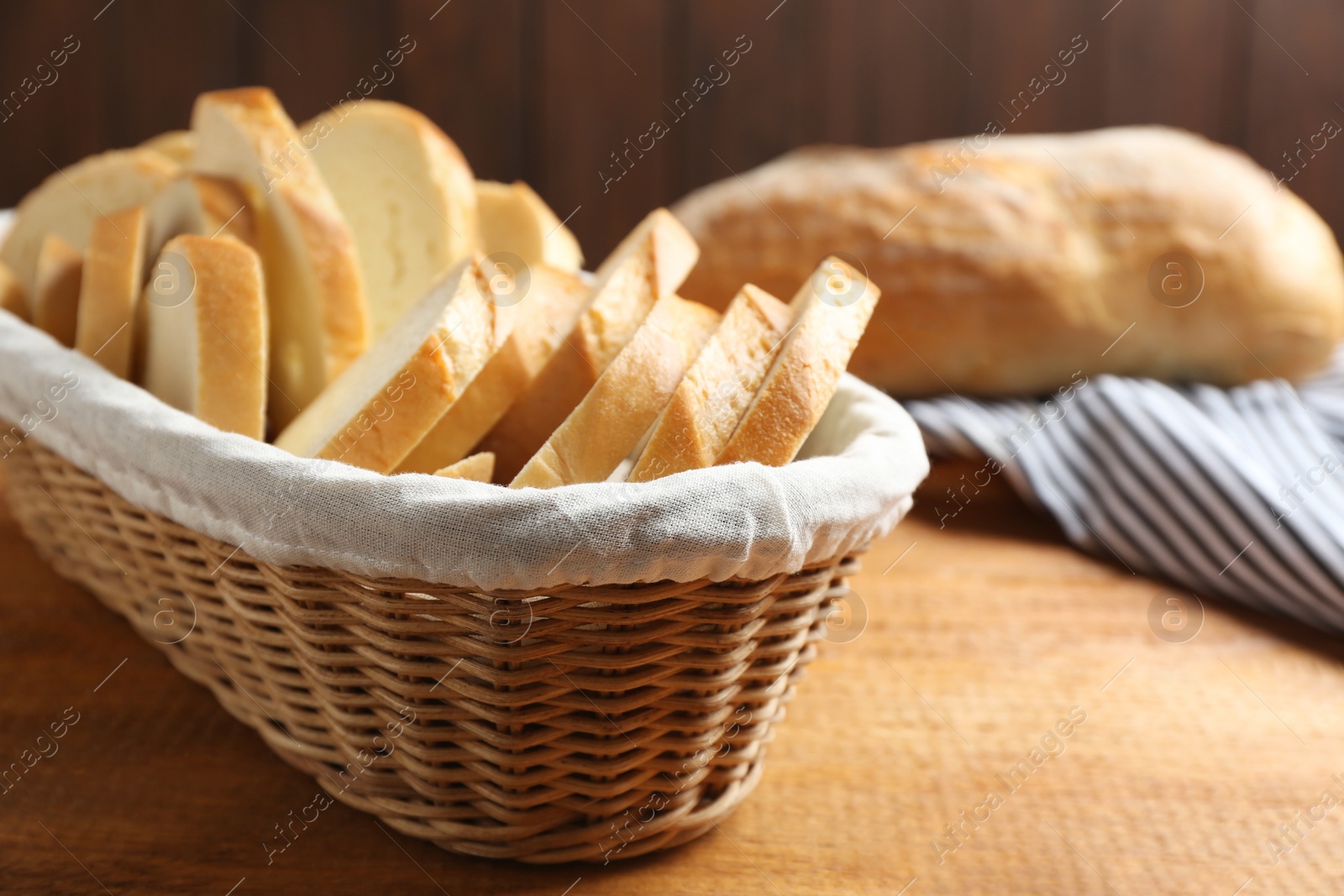 Photo of Slices of tasty fresh bread in wicker basket on wooden table, closeup