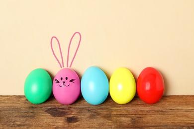 One eggs with drawn face and ears as Easter bunny among others on wooden table against beige background