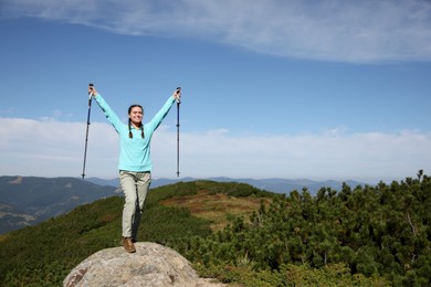 Photo of Hiker with trekking poles standing on rocky peak in mountains