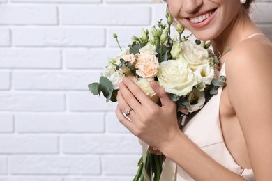 Young bride with beautiful wedding bouquet near white brick wall, closeup. Space for text