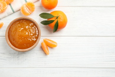 Flat lay composition with tasty tangerine jam on white wooden table. Space for text