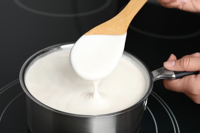 Photo of Woman cooking delicious creamy sauce in pan on stove, closeup
