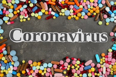 Word CORONAVIRUS and different pills on grey stone background, flat lay