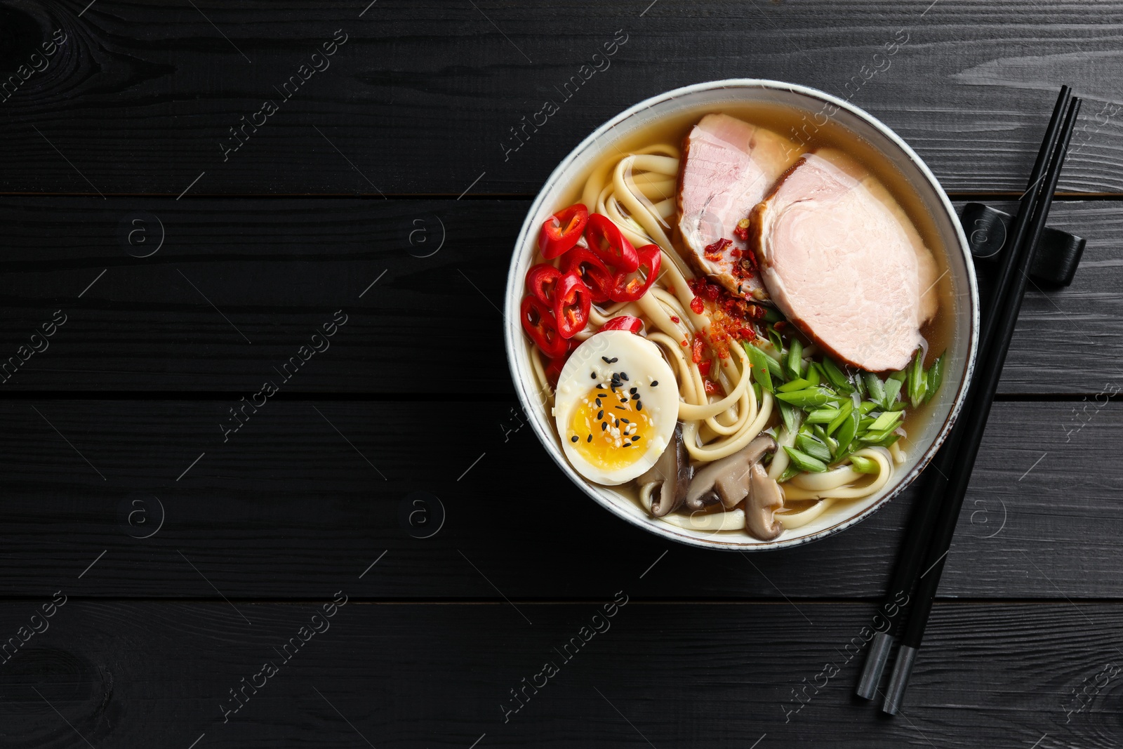 Photo of Delicious ramen in bowl and chopsticks on black wooden table, flat lay with space for text. Noodle soup