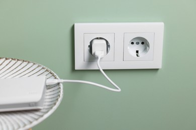 Photo of Power bank plugged into electric socket on light green wall