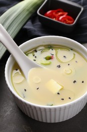 Photo of Bowl of delicious miso soup with tofu and spoon on grey table, closeup