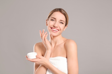 Young woman with jar of body cream on color background