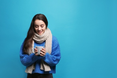 Young woman in sweater with cup of hot coffee on color background, space for text. Winter season