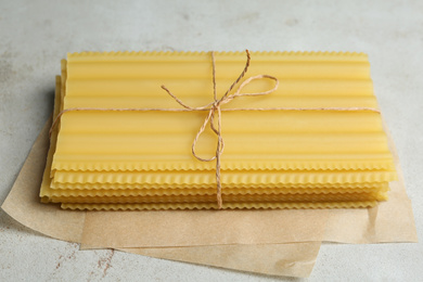 Uncooked lasagna sheets tied with rope on light grey table, closeup