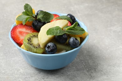 Photo of Tasty fruit salad in bowl on gray textured table, closeup. Space for text
