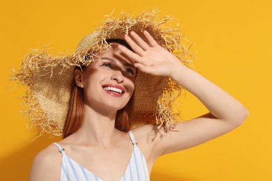 Photo of Beautiful young woman in straw hat shading herself with hand from sunlight on orange background