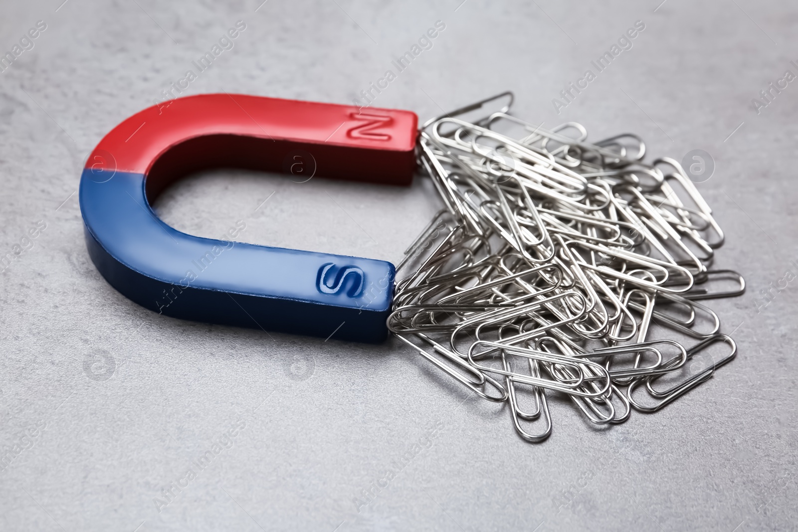 Photo of Magnet attracting paper clips on grey background