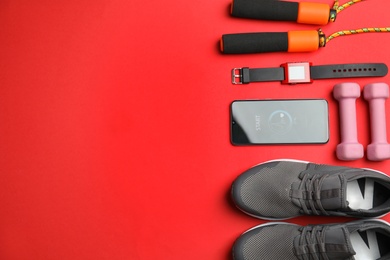 Photo of Smartphone with heart rate monitor app and fitness accessories on red background, flat lay. Space for text