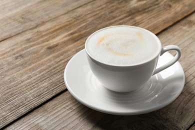 Tasty cappuccino in coffee cup on wooden table, closeup. Space for text