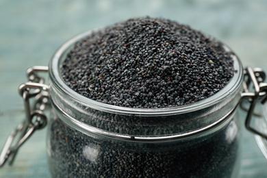 Photo of Poppy seeds in glass jar on blue table, closeup