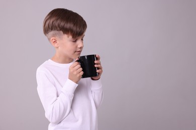 Photo of Cute boy drinking beverage from black ceramic mug on light grey background, space for text