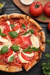 Photo of Delicious Caprese pizza on black wooden table, flat lay
