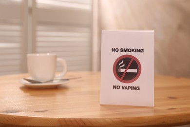 Photo of No Smoking sign and cup of drink on wooden table indoors, selective focus