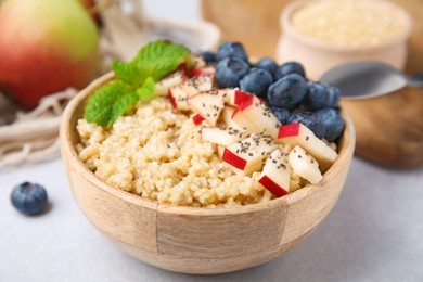 Bowl of delicious cooked quinoa with apples, blueberries and chia seeds on light grey table, closeup