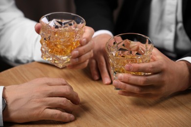 Men with glasses of whiskey at wooden table indoors, closeup
