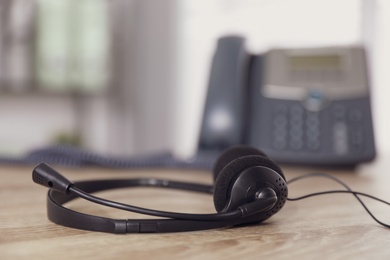 Photo of Headset on wooden table in office, closeup with space for text. Hotline service