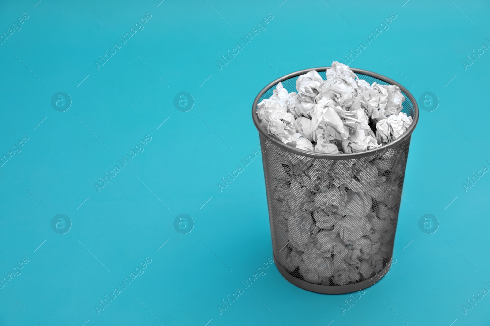 Photo of Metal bin with crumpled paper on color background, space for text