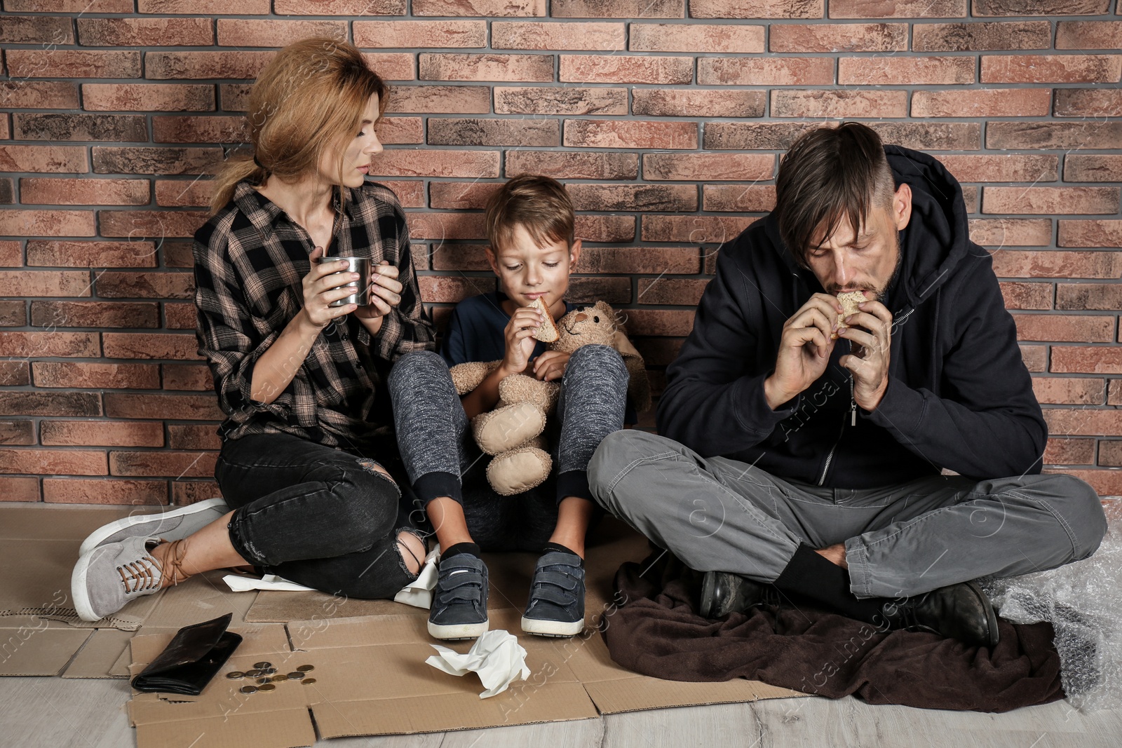 Photo of Poor homeless family sitting on floor near brick wall