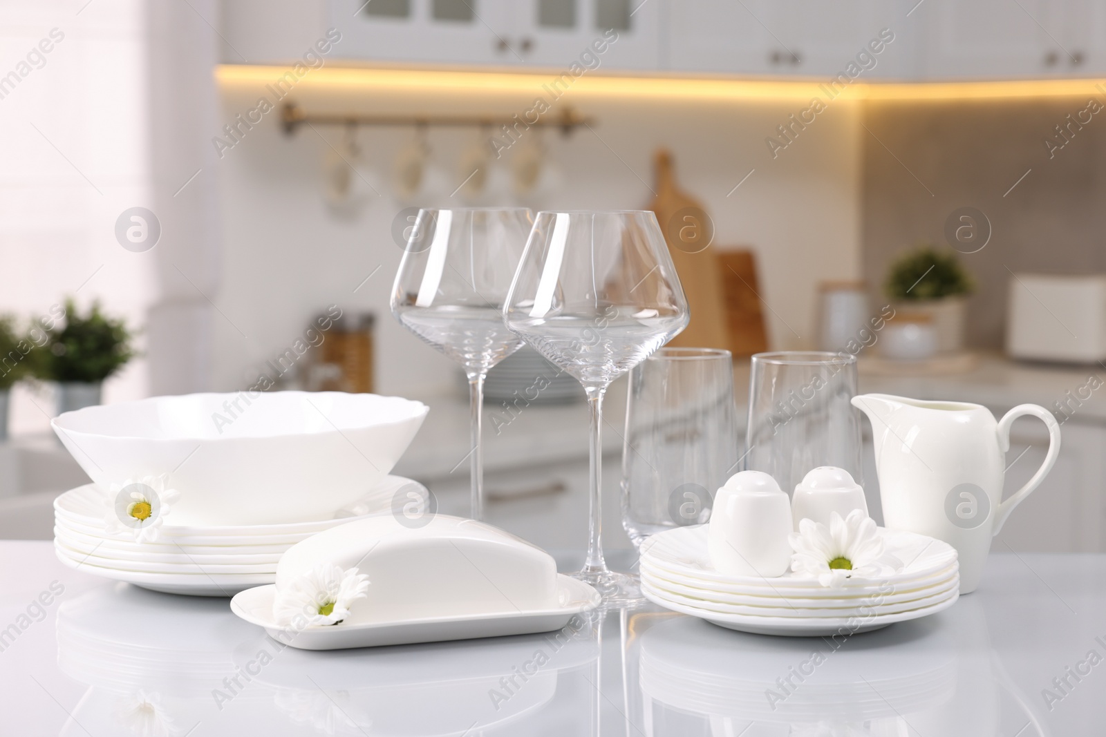 Photo of Set of clean dishware, glasses and flowers on table in kitchen