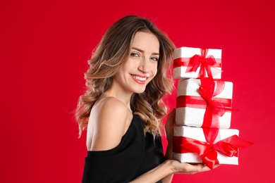 Beautiful young woman with Christmas presents on red background