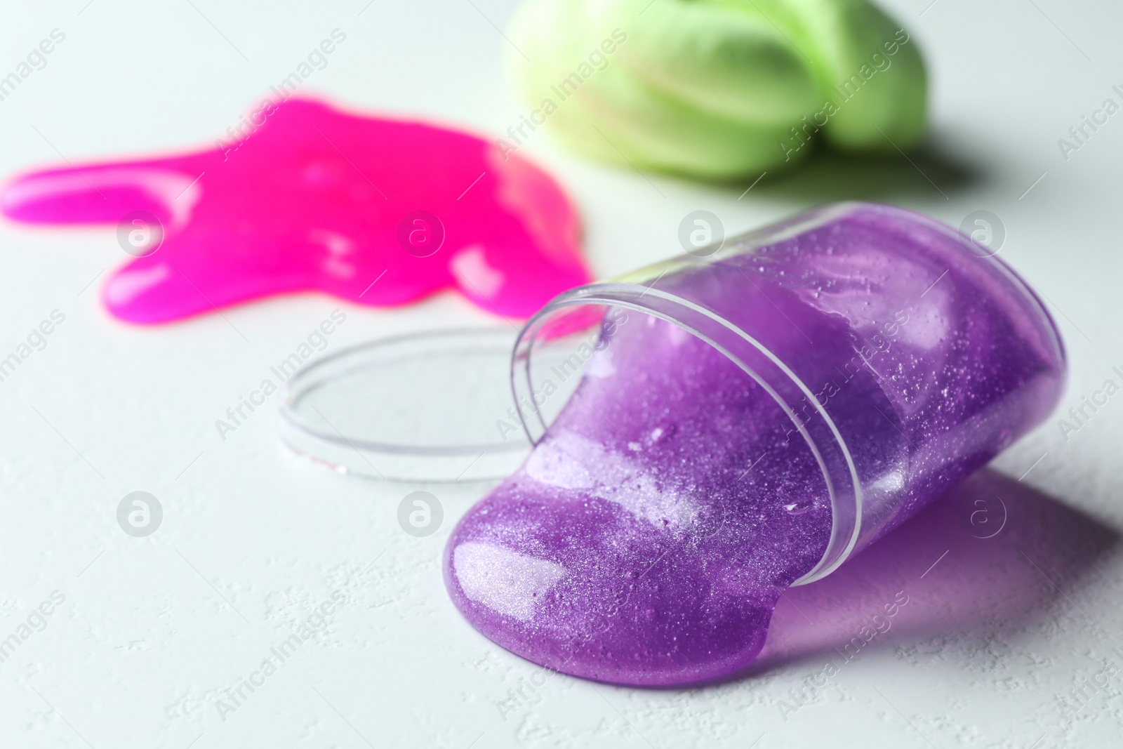 Photo of Overturned plastic container with purple slime on white background. Space for text