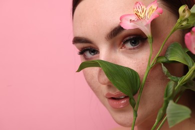 Photo of Beautiful woman with fake freckles and flower on pink background, closeup. Space for text