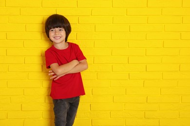 Cute little boy near yellow brick wall, space for text