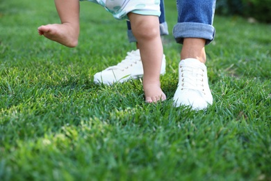 Photo of Cute little baby learning to walk with his nanny on green grass outdoors, closeup