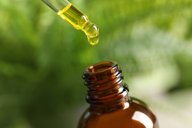 Photo of Pipette with oil over bottle on blurred background