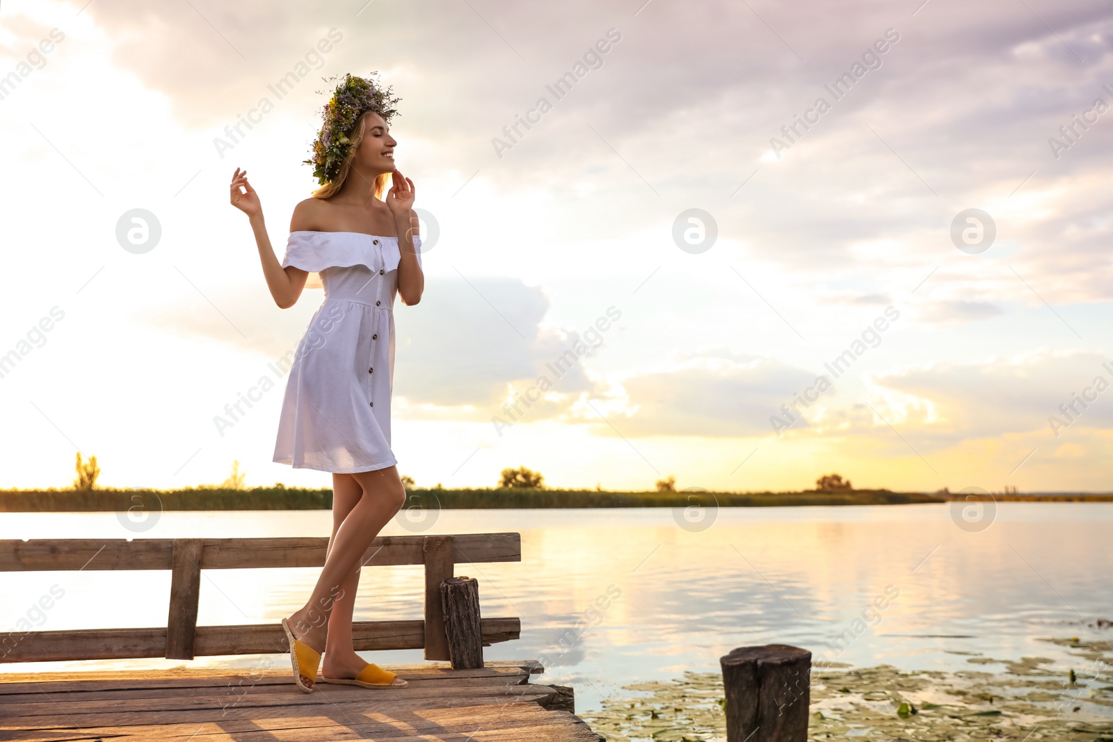 Photo of Young woman wearing wreath made of beautiful flowers on pier near river