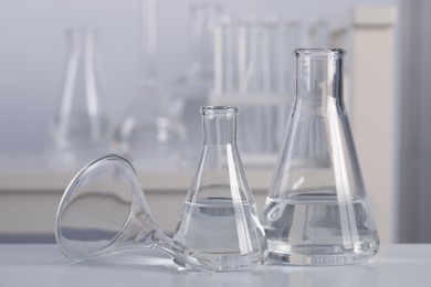 Photo of Conical flasks with transparent liquid and funnel on table in laboratory