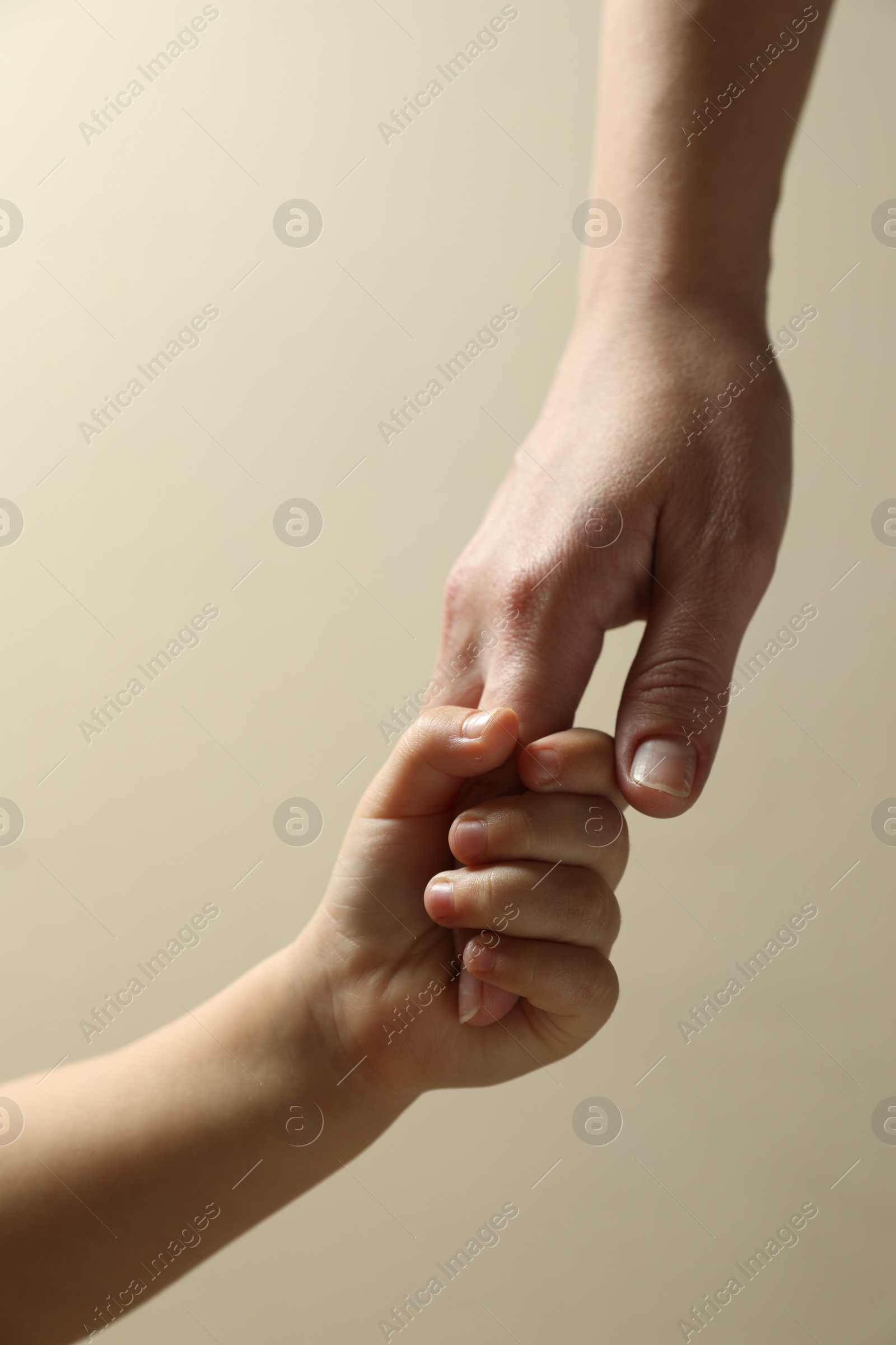 Photo of Mother and child holding hands on beige background, closeup