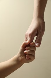 Mother and child holding hands on beige background, closeup