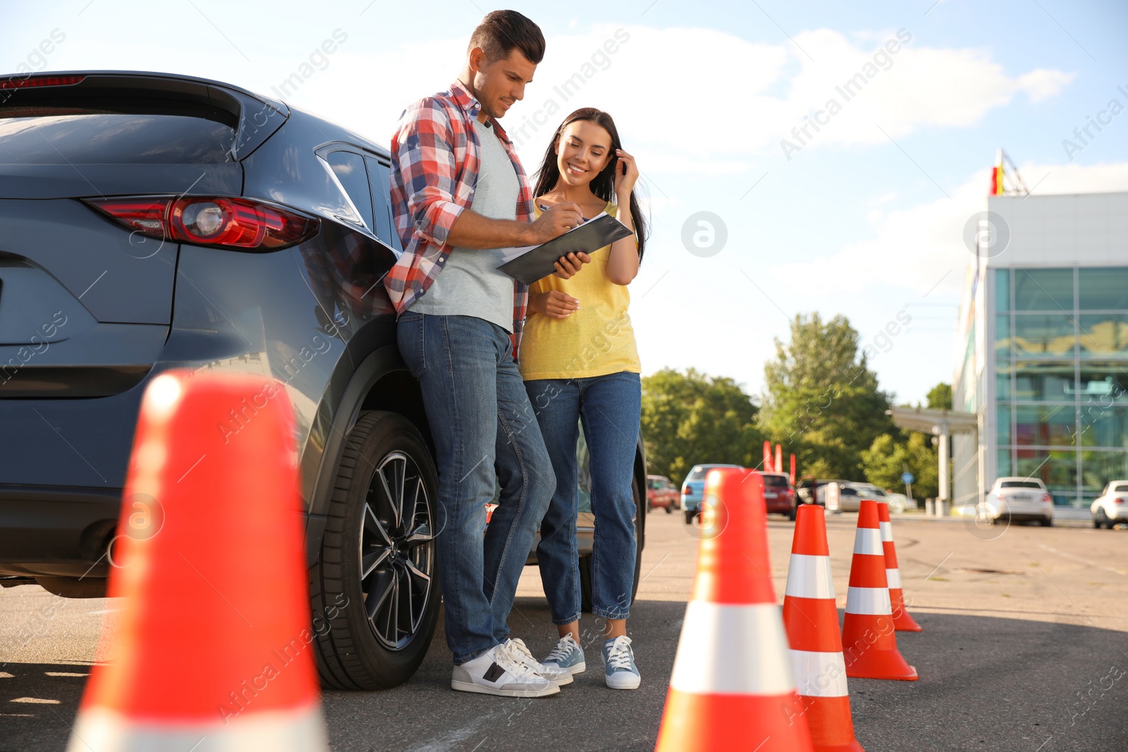 Photo of Instructor with clipboard and his student near car outdoors. Driving school exam