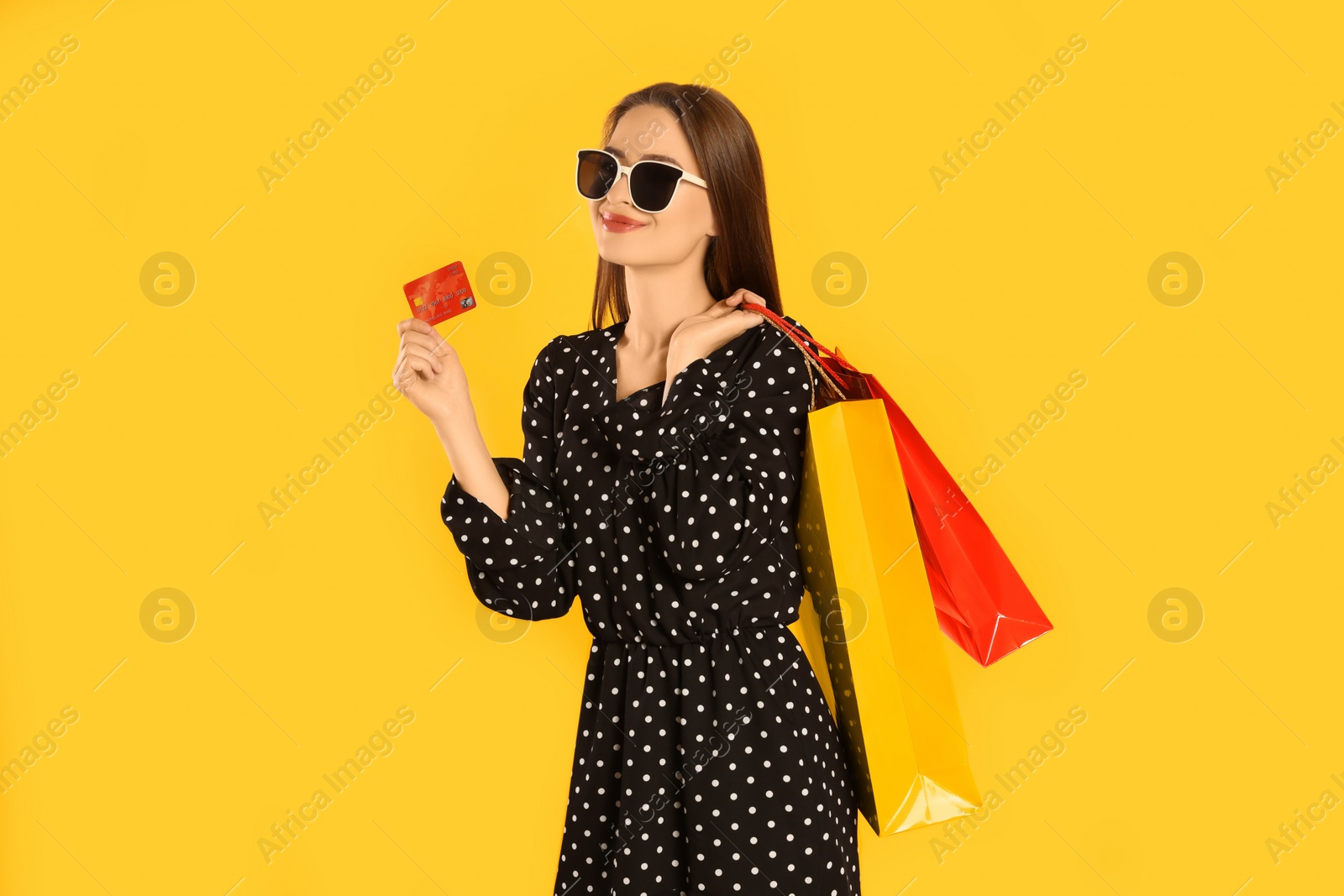 Photo of Happy young woman with shopping bags and credit card on yellow background. Big sale