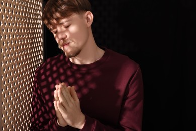 Photo of Man praying during confession near wooden window in booth. Space for text