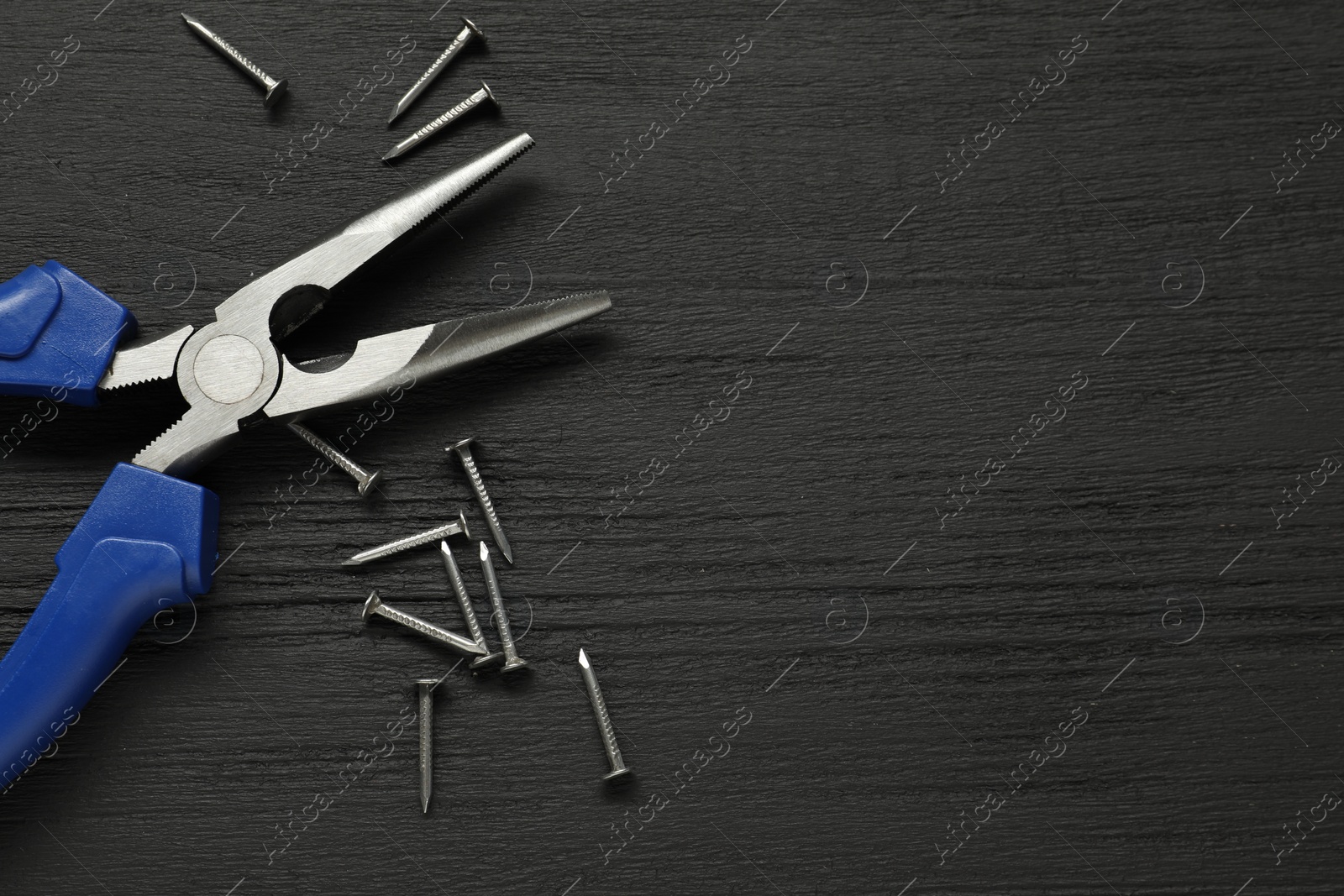 Photo of Needle nose pliers and nails on black wooden table, flat lay. Space for text